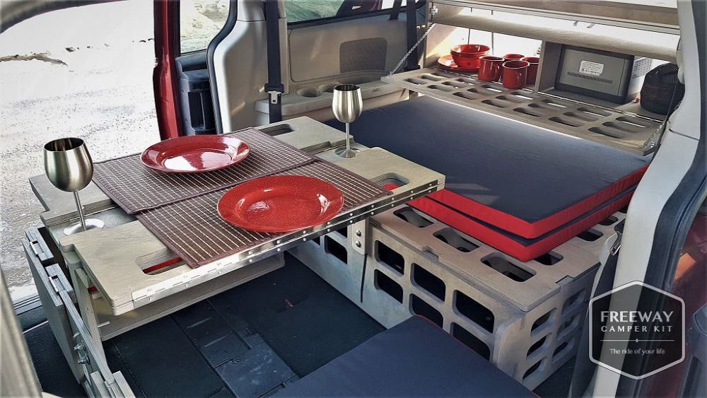 Interior view of minivan converted with Freeway camper kit shows dish storage, and a multi functional folding table with set for a meal.