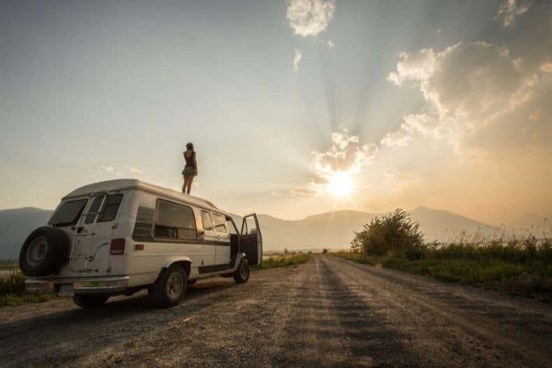 Woman stands on top of used camper van watching sunset