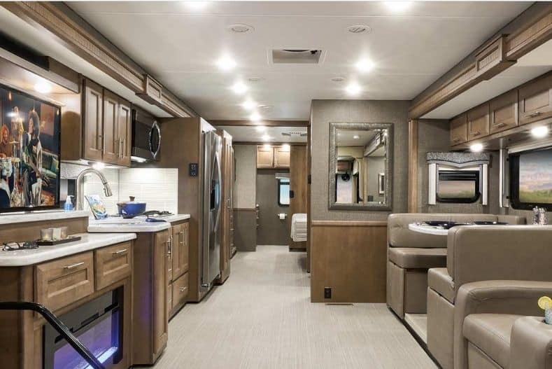 Thor Motor Coach Challenger 37DS Class A motorhome with bunks interior view with brown, beige and natural wood tones. Dinette and recliners partially show to the right of frame, kitchenette to the left and bedroom and bathroom hidden near the rear