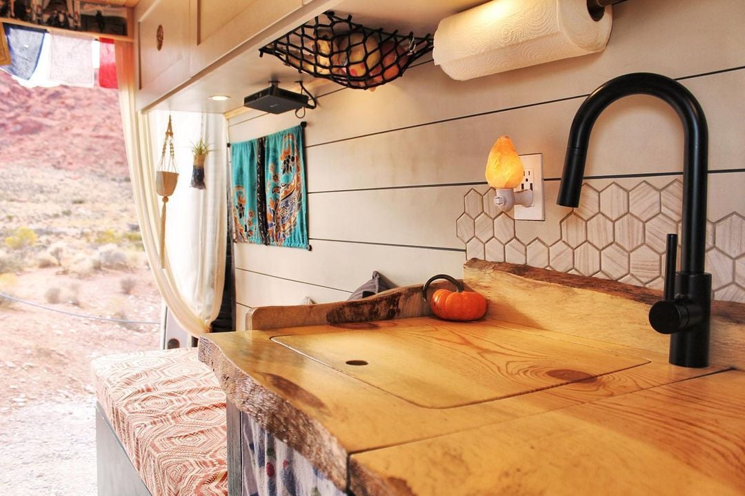 A campervan kitchen with warm wood counters, an elastic net for storage and a lantern