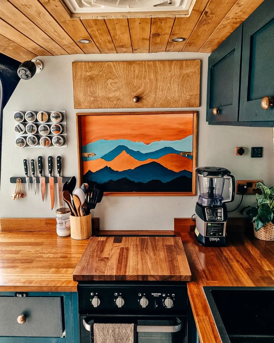 A campervan kitchen wall with spice jars on a rack and a painting of mountains