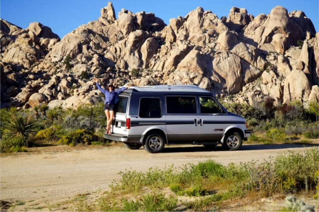 Woman standing on back of a Chevy Astro Van, a super affordable camper van