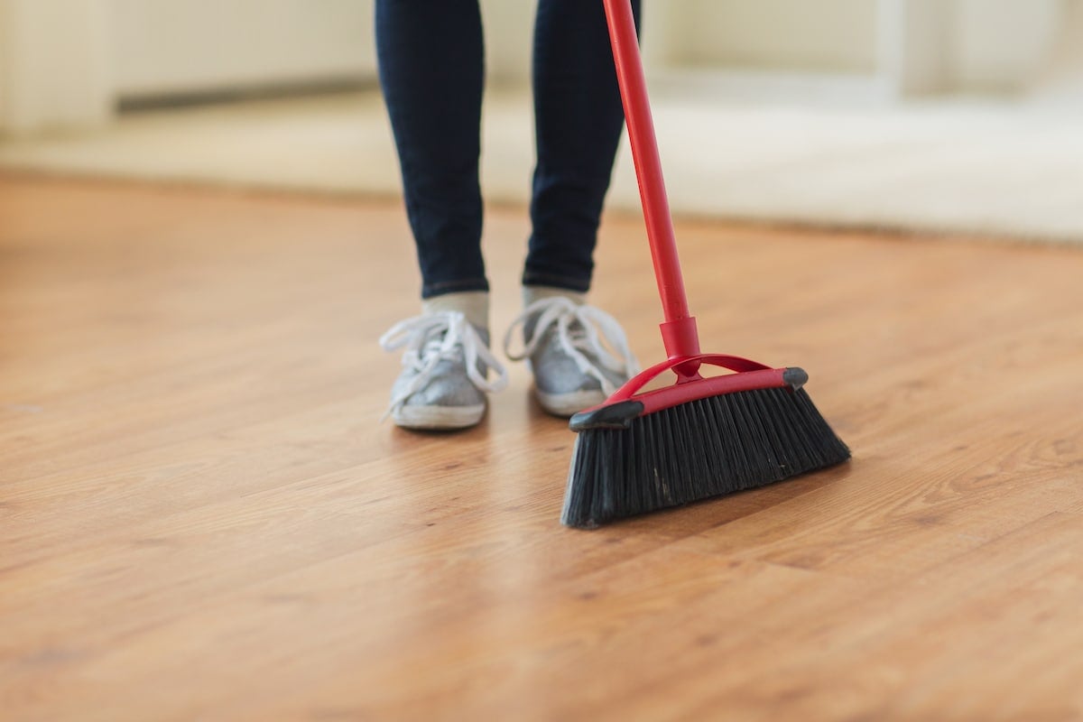 A person's legs wearing black leggings with tennis shoes on with a red broom on a hardwood floor.