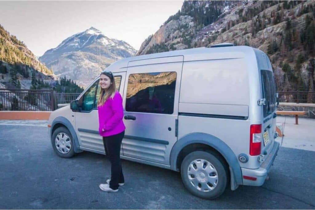 Woman standing next to a Ford Transit connect, an awesome affordable camper van