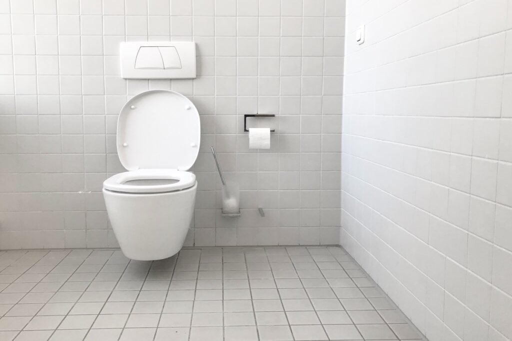 A white toilet inside of a tiled white bathroom.