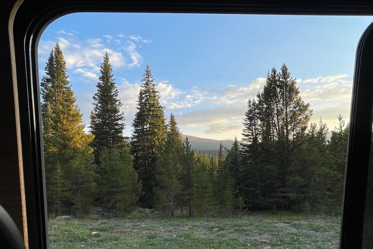 Trees with a mountain peeking behind them with a blue sky and clouds, framed within the outline of a window.