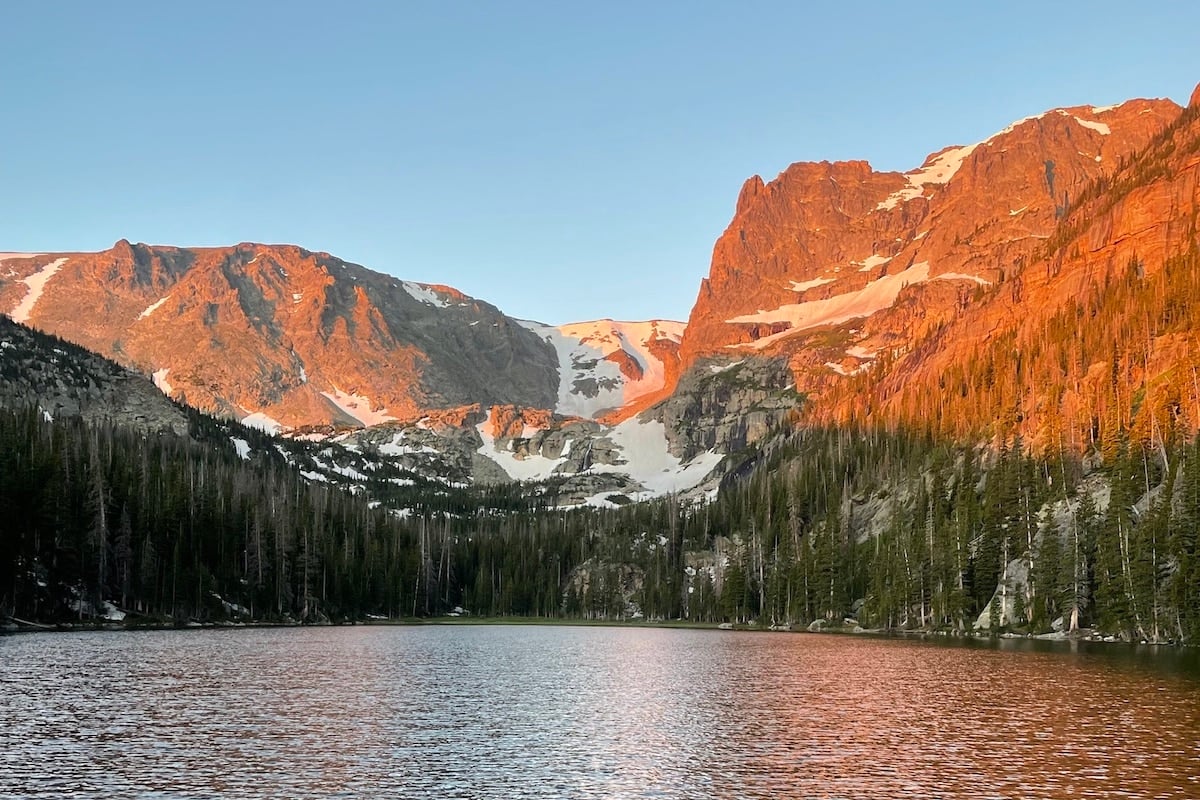 Sunrise at Odessa Lake in Rocky Mountain National Park. There is snow on mountains and water in front.