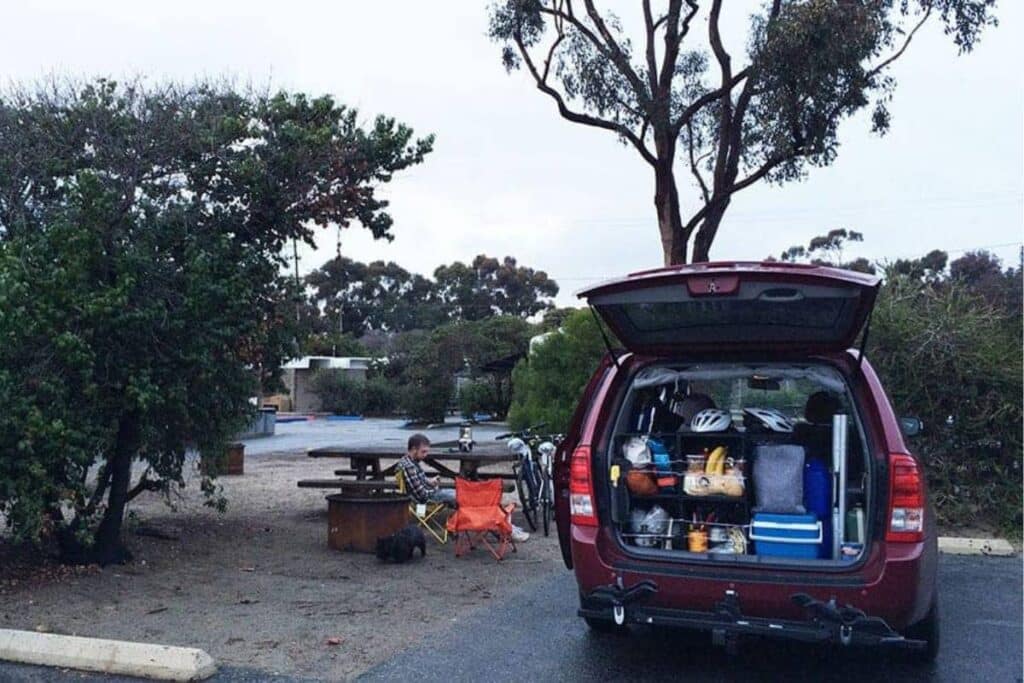 minivan camper showing its interior parked outdoors while the owner is sitting outside