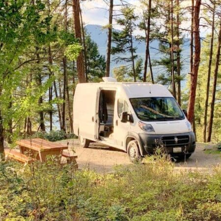 Dodge Ram Promaster RV Rental parked in a forested campsite by a picnic table