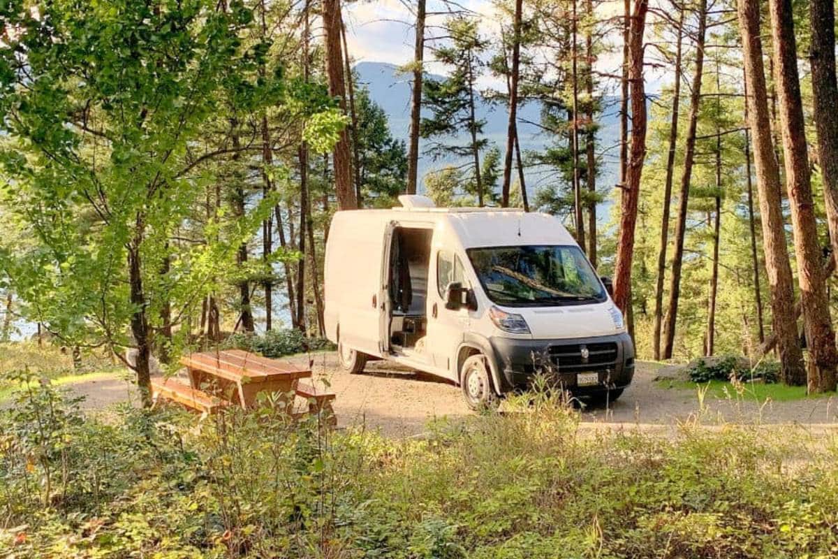 Dodge Ram Promaster RV Rental parked in a forested campsite by a picnic table