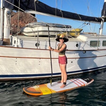 woman standing on a paddleboard next to a sailboat