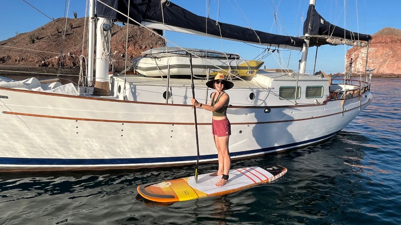 woman standing on a paddleboard next to a sailboat