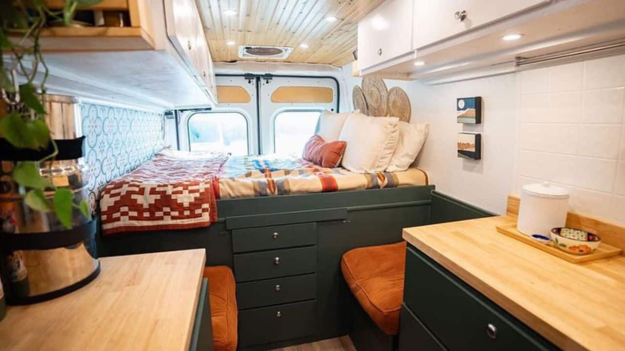 A campervan interior with a platform bed, a wood kitchen and warm lighting