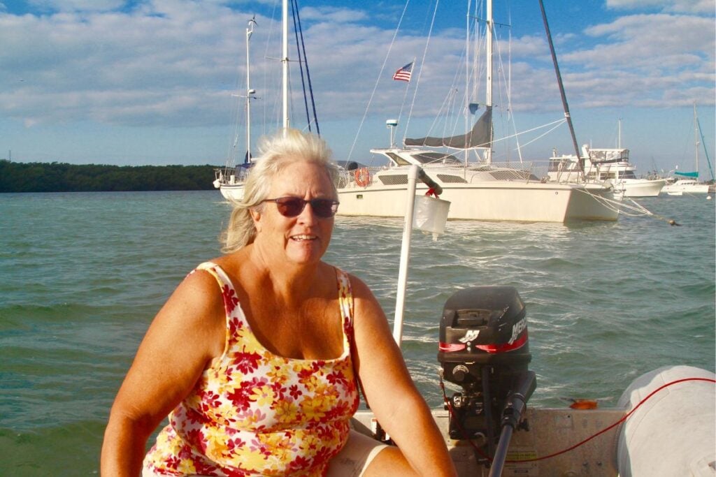 woman in a dinghy with a catamaran behind her