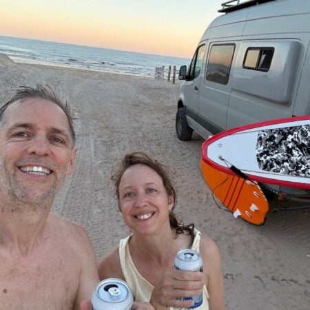 man and woman holding beers outside campervan