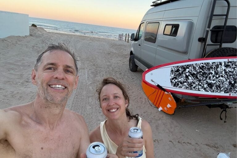 man and woman holding beers outside campervan