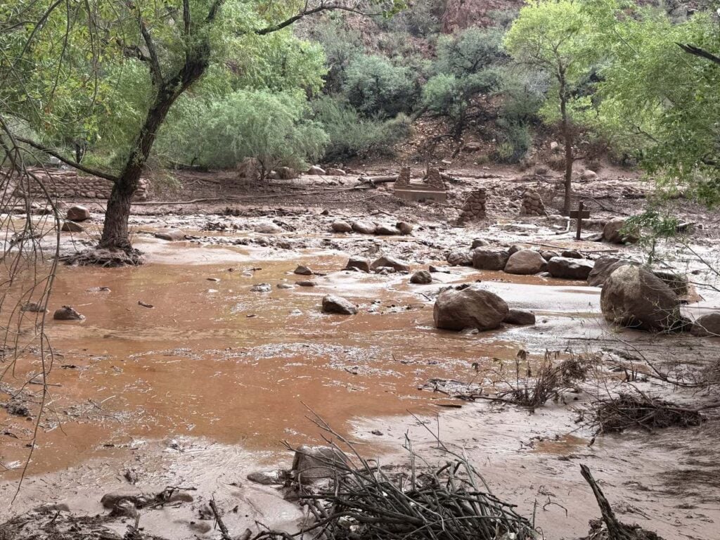 Muddy floodwater and debris cover the Bright Angel Creek corridor after the August 29 flash flood, with only stone bridge pylons left standing