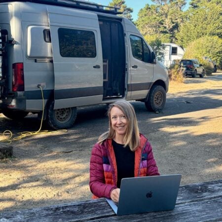 woman working on laptop with campervan in the background