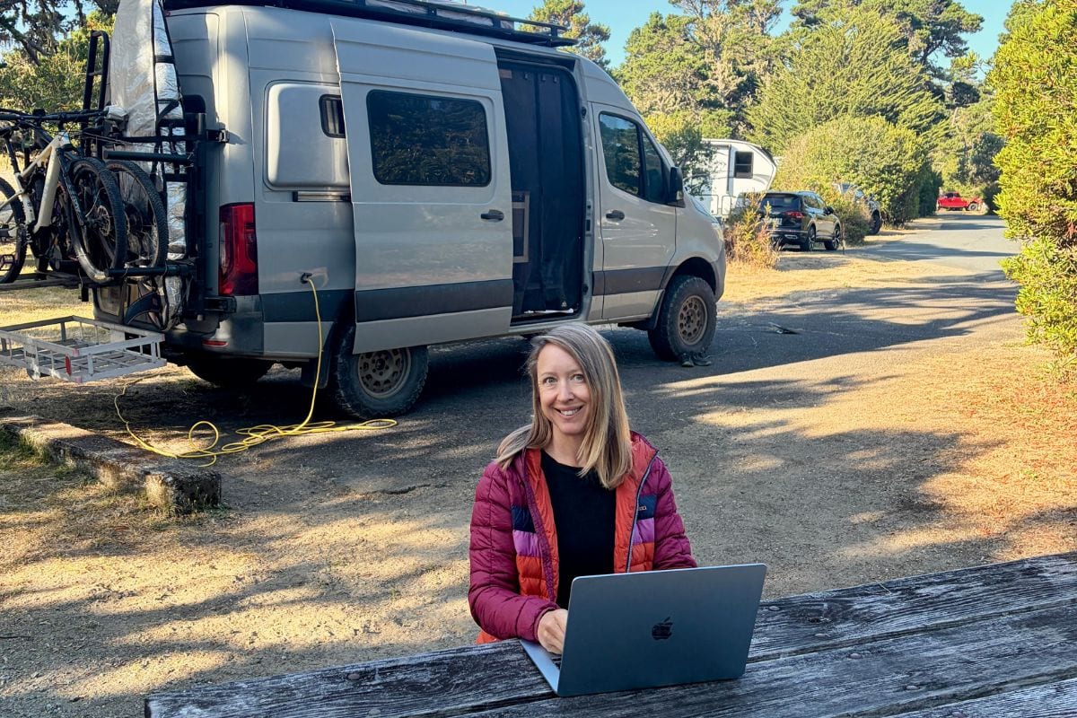 woman working on laptop with campervan in the background