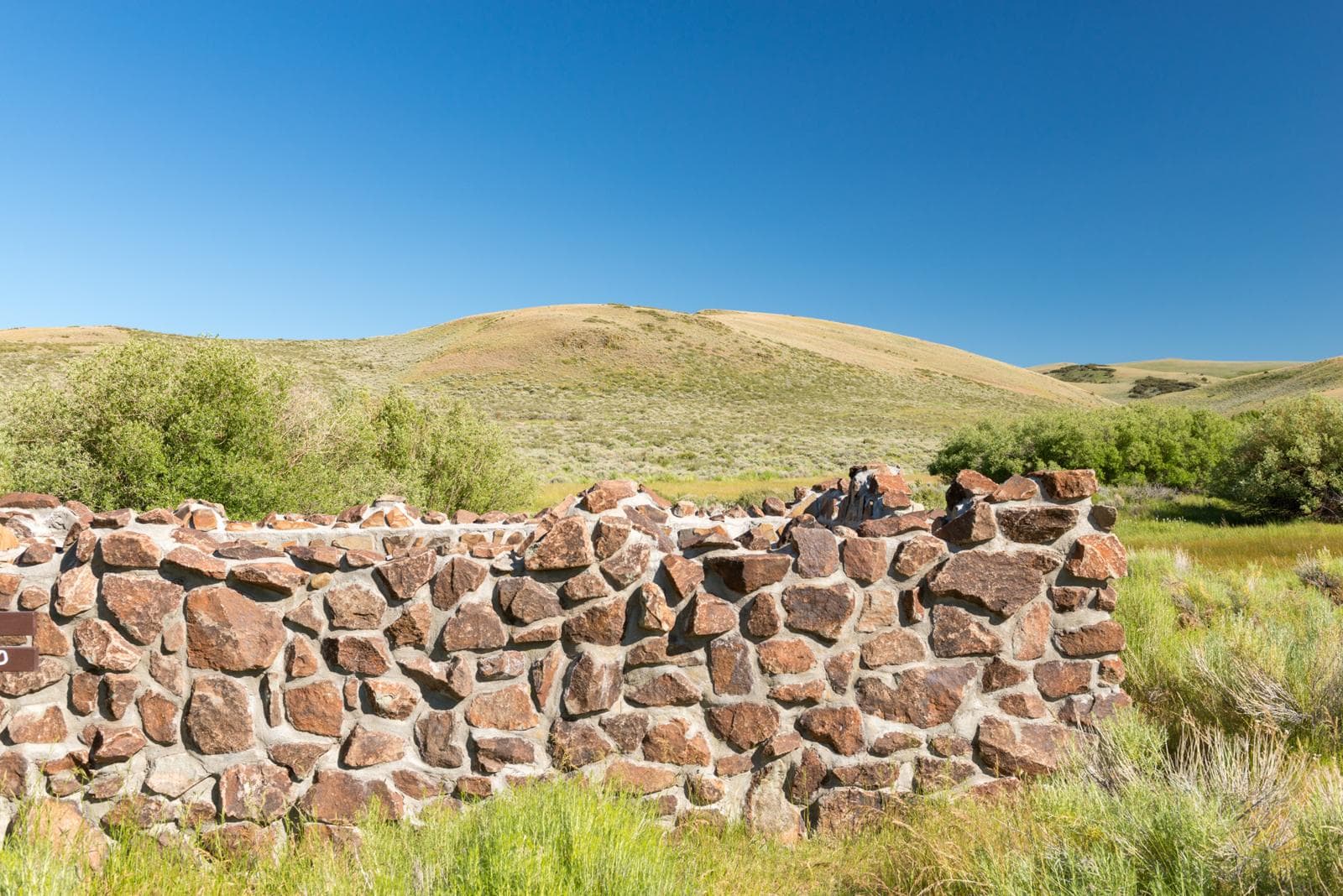Stone wall enclosing the hot springs pool, grassy hills, blue sky, Hart Mountain Hot Springs