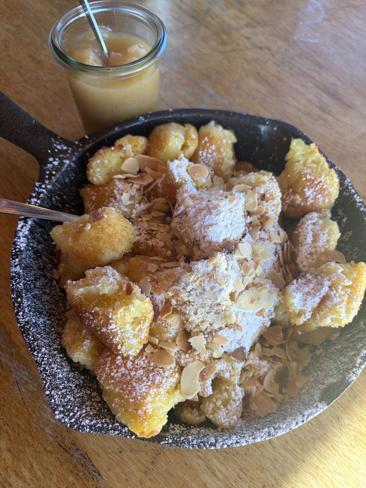 A bowl of Kaiserschmarrn-style shredded pancake with powdered sugar and a jar of applesauce at a mountain hut