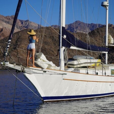 Kristin standing on the bow of a sailboat at anchor in a Baja cove with desert mountains behind