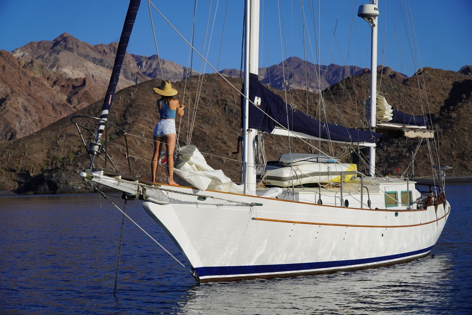 Kristin standing on the bow of a sailboat at anchor in a Baja cove with desert mountains behind