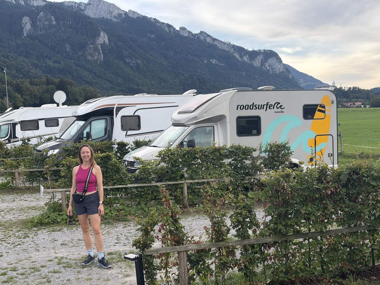 Kristin standing beside the Roadsurfer Van Villa campervan at a Bavarian campground with mountains behind