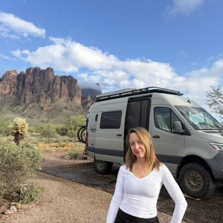 Kristin Hanes standing beside her Sprinter van at a desert campsite below the Superstition Mountains