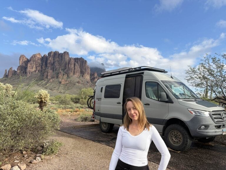 Kristin Hanes standing beside her Sprinter van at a desert campsite below the Superstition Mountains