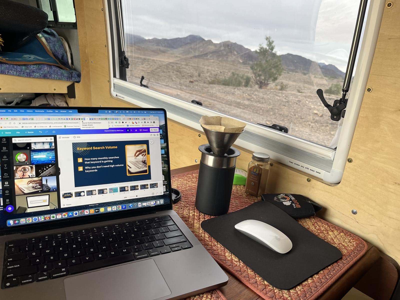 A laptop and a coffee grinder at a campervan window desk with the desert outside