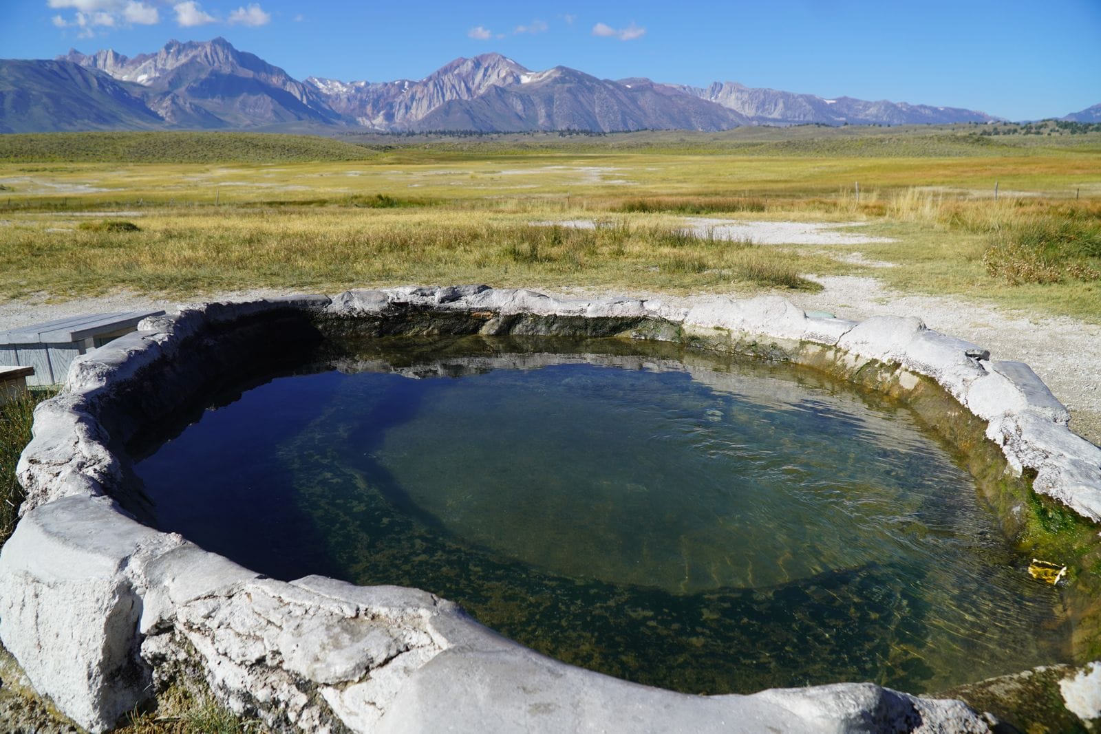 A round stone-rimmed hot spring tub with the Sierra Nevada behind, Long Valley, California