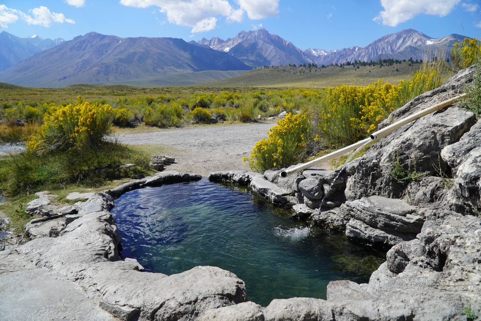A rock hot spring tub fed by a pipe, rabbitbrush in bloom, Long Valley near Mammoth Lakes