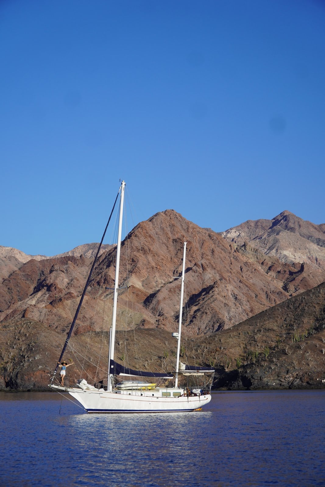A sailboat at anchor in a calm Baja cove under bare desert mountains