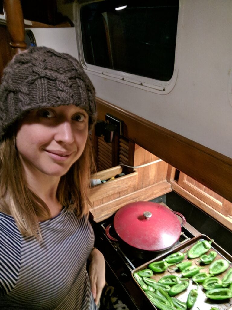 Kristin cooking in the galley of her sailboat in a wool beanie, a pressure cooker on the stove