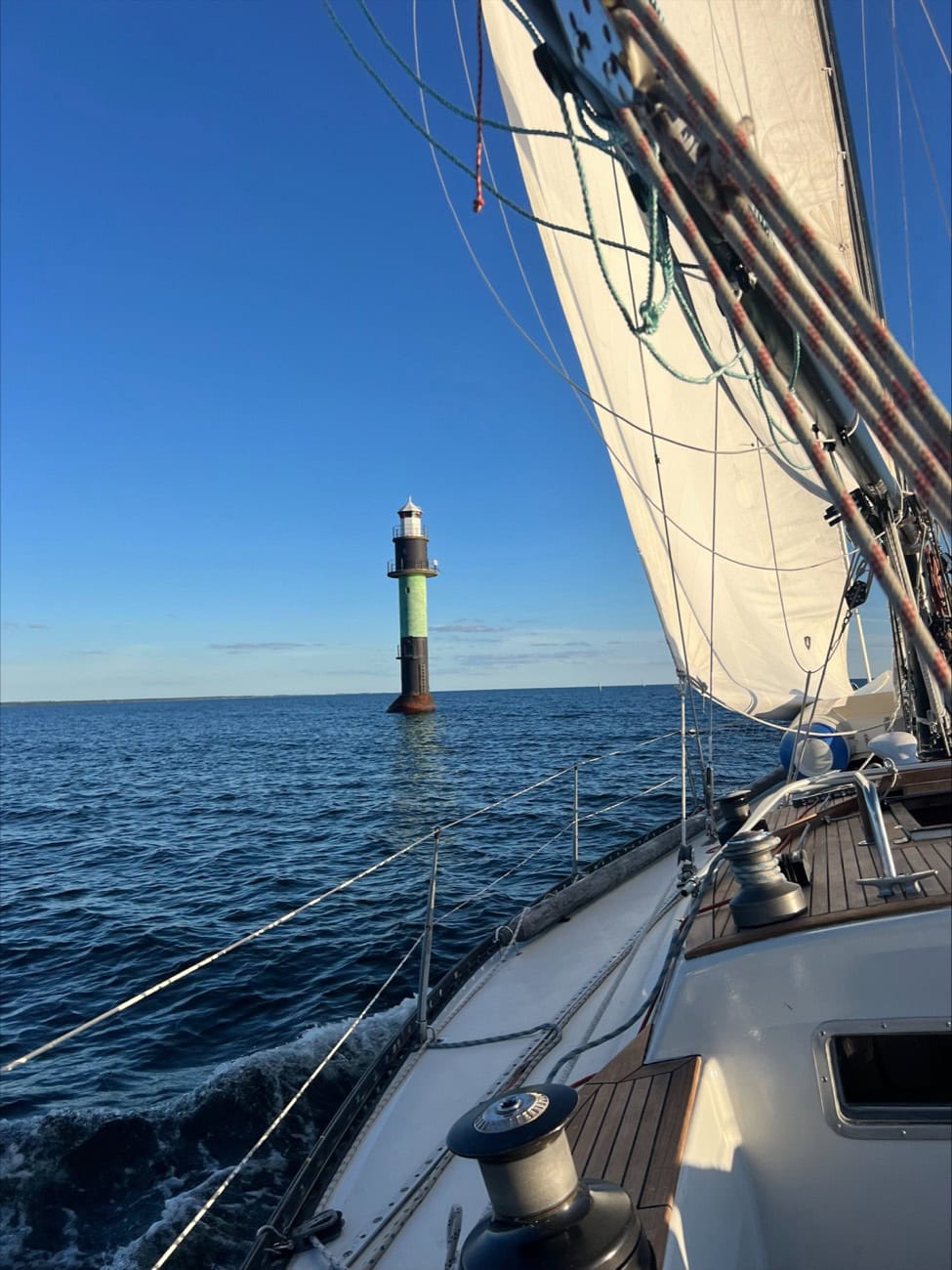 A green lighthouse seen past a sailboat's mainsail on a clear day