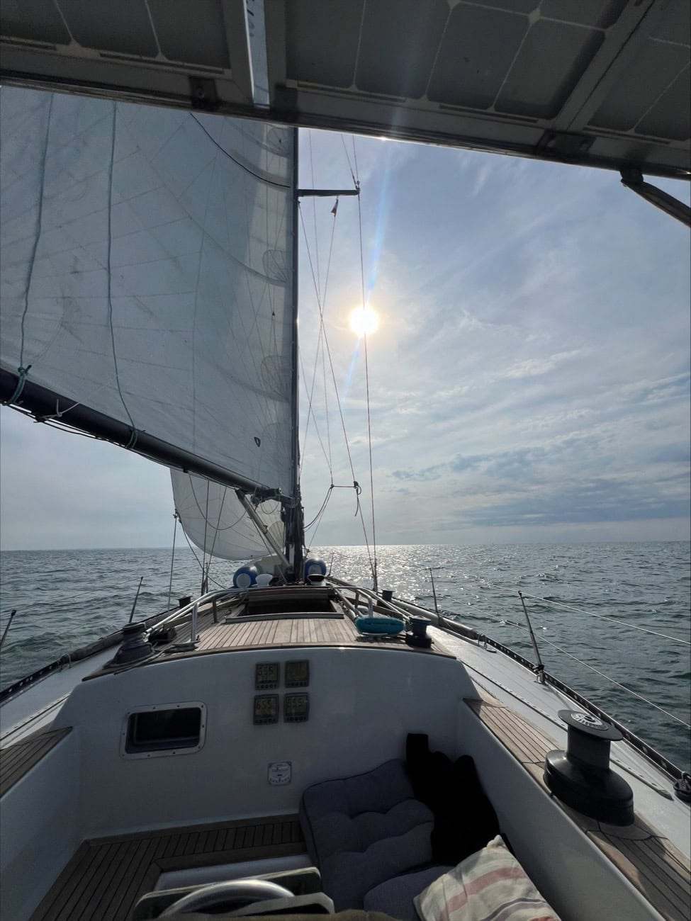A sailboat's sails against the afternoon sun over the sea