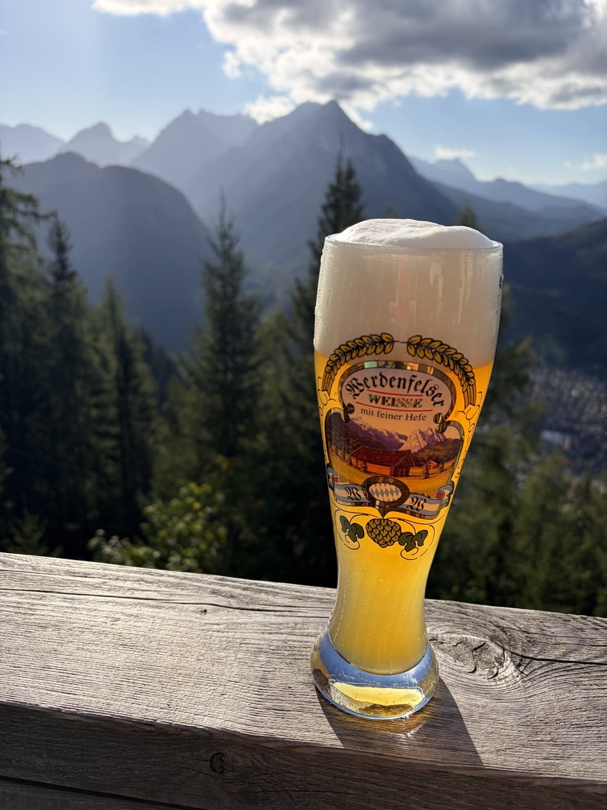 A glass of wheat beer on a mountain hut balcony with the valley and mountains behind