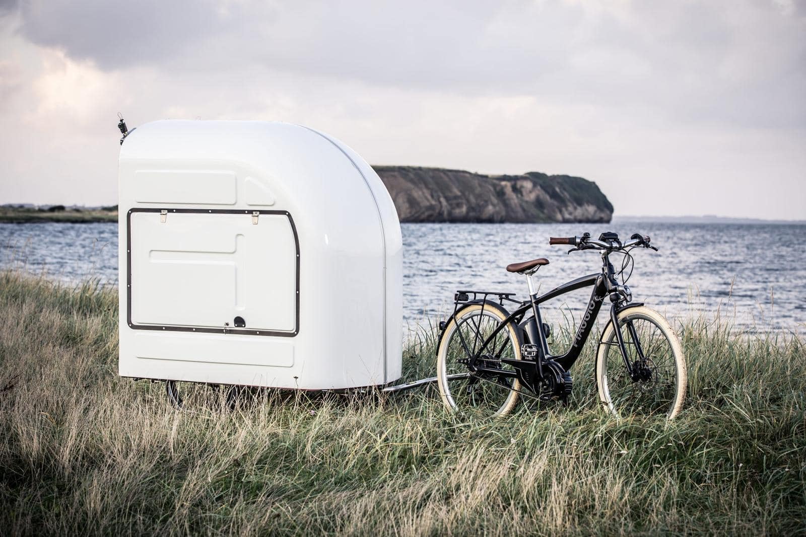 The Wide Path bicycle camper parked by the sea with a bike beside it